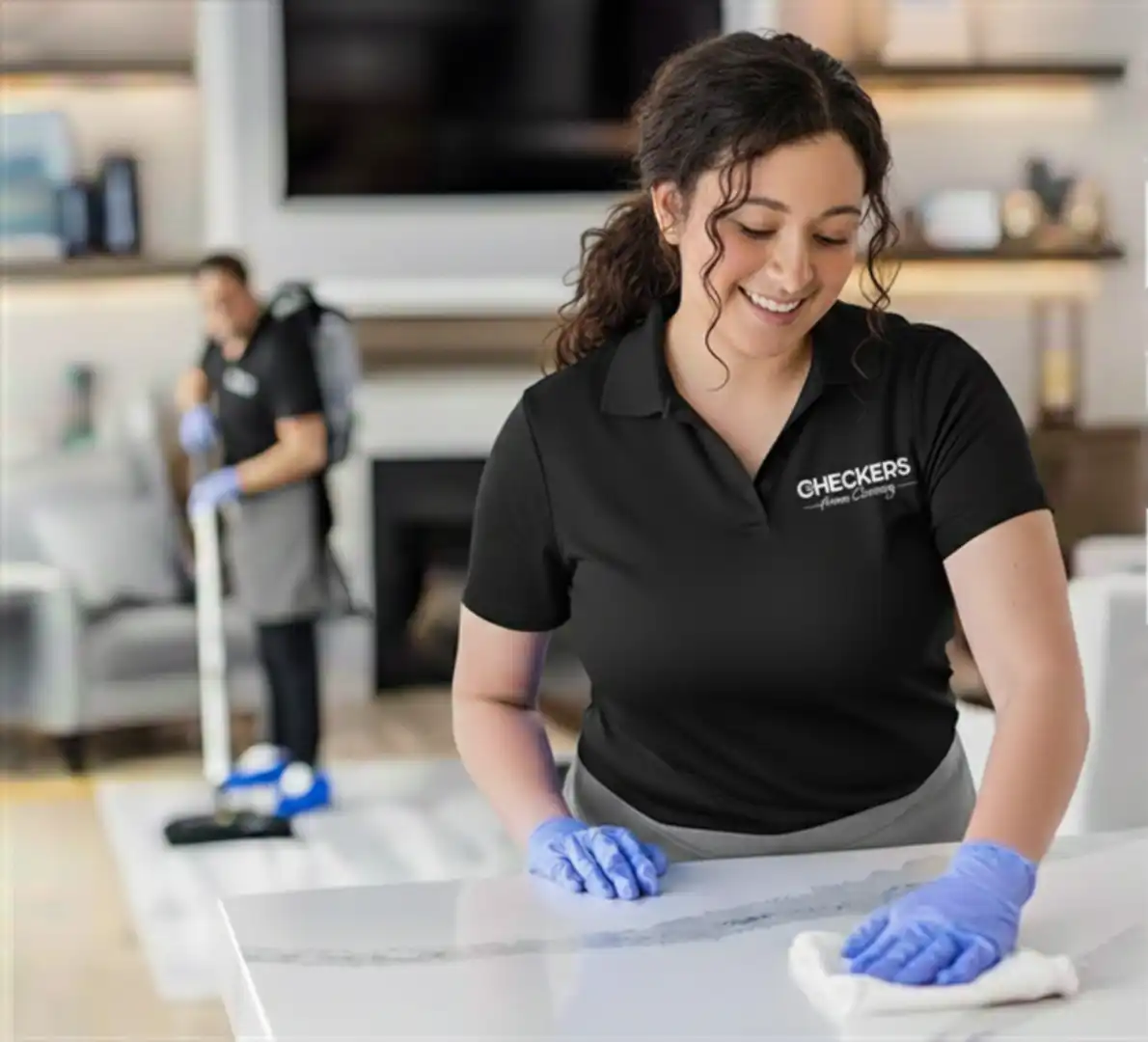 Two Checkers Home Cleaning employees at work; one wipes kitchen counters, the other vacuums a living room rug in Sioux City, Iowa